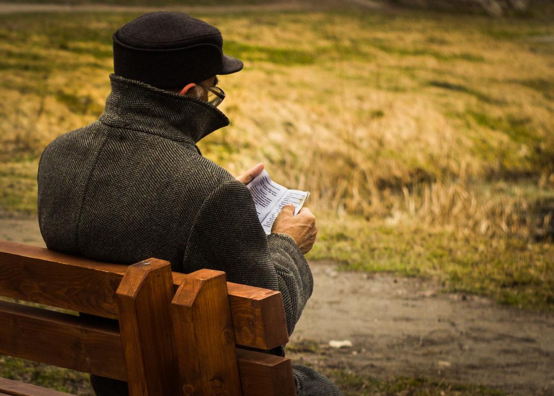 older man sitting on bench reading a book
