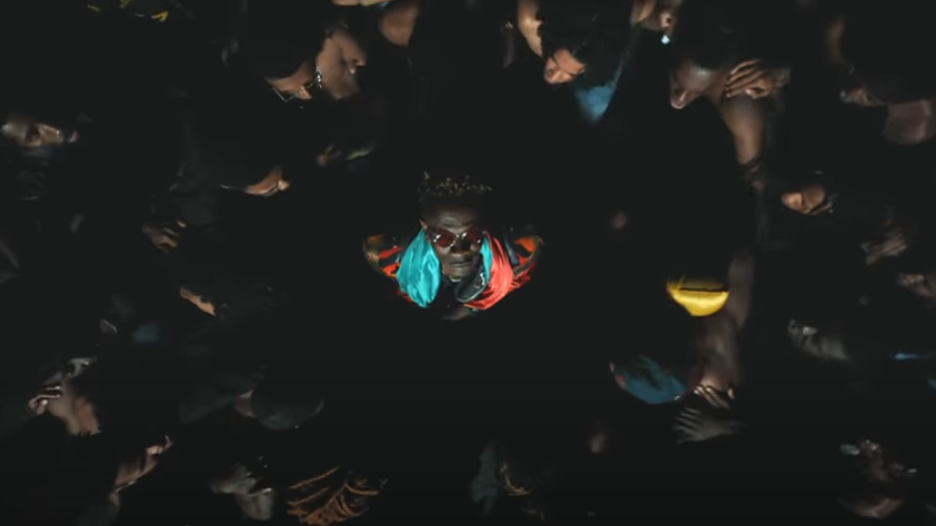 Shatta Wale with a Ghana flag around his neck facing up to the camera in the music video for Already with Beyonce