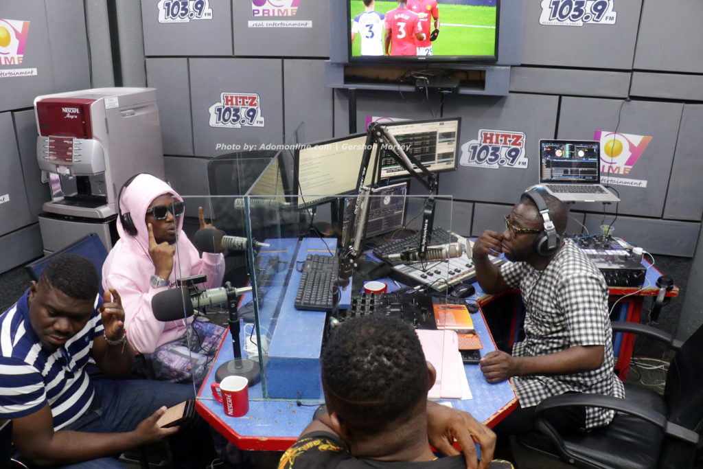 Flyboy Gee (pink hoodie) seated for an interview on Daybreak Hitz show with Andy Dosty (checked shirt)