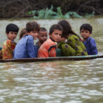 A man helps children navigate floodwaters using a satellite dish in Balochistan, Pakistan, on Friday, August 26.