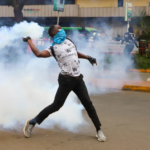 A protester throws a tear gas canister back at police officers during a protest over proposed tax hikes in Nairobi, Kenya on June 20, 2024 [Andrew Kasuku/AP]